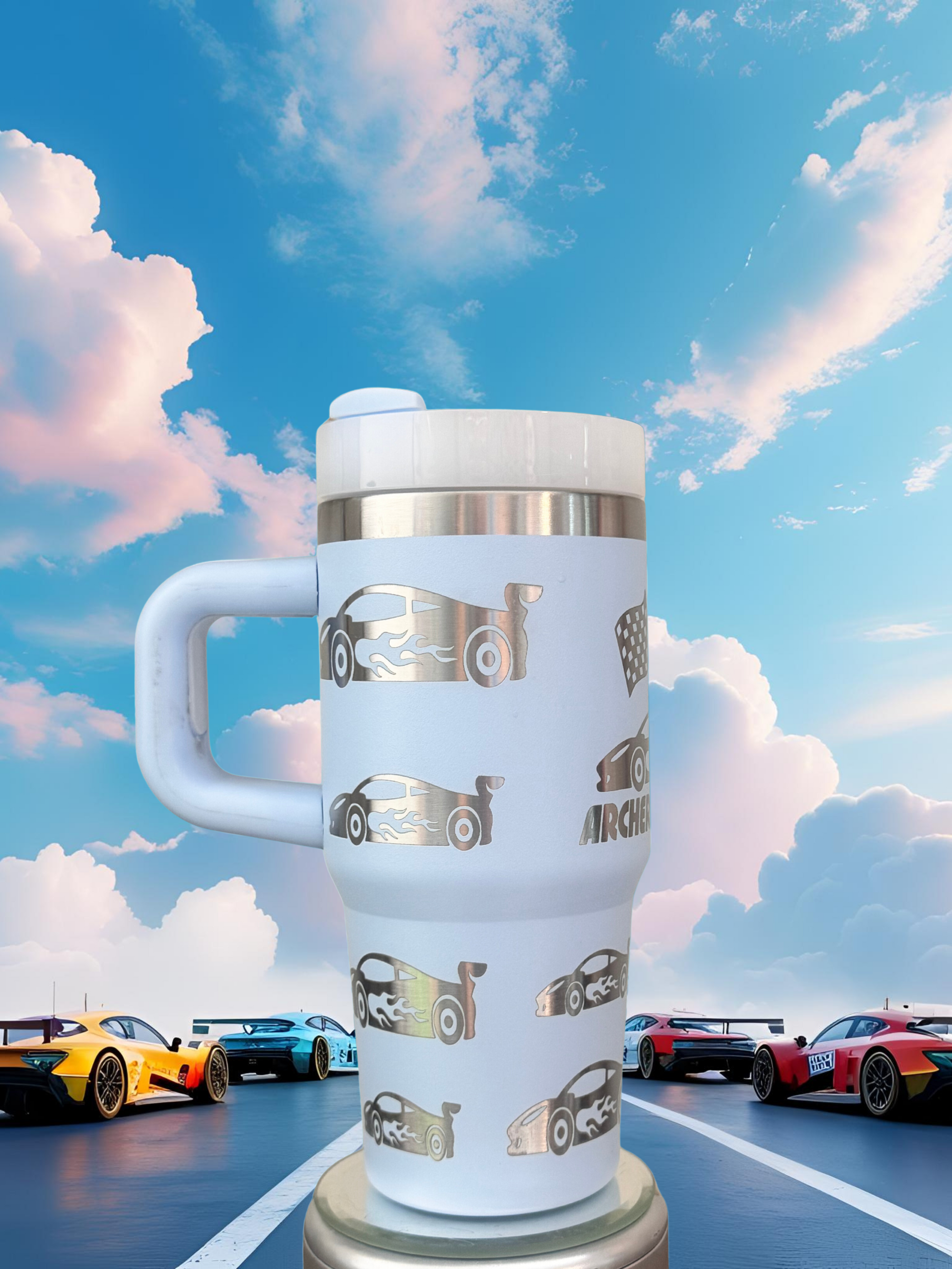 A white thermos mug with a silver handle and a design of cars printed on it, placed on a surface with other cars in the background.